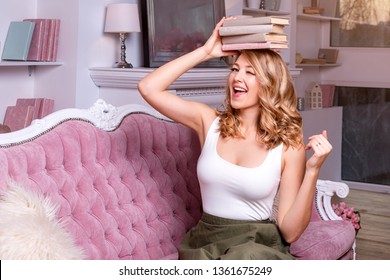 Female student balancing books on top of her head and winking. Beautiful blonde girl keeps a stack of books on her head. Concept of education, courses, examinations, homework, list of books to read.