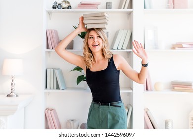 Female student balancing books on top of her head. Beautiful blonde girl keeps a stack of books on her head. The concept of education, courses, examinations, homework, list of books to read.