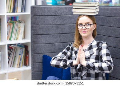 Female student balancing books on her head. Beautiful blonde with glasses, the girl holds a stack of books on her head. Education concept, courses, exams, homework, list of books to read.