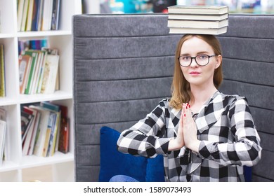 Female student balancing books on her head. Beautiful blonde with glasses, the girl holds a stack of books on her head. Education concept, courses, exams, homework, list of books to read in the librar