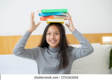 Female student balancing books on her head, Beautiful girl holds a stack of books on her head and smiles. Education concept, studying with books.