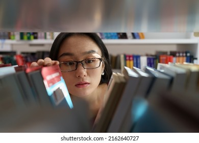 Female Student Choosing Book From Bookshelf In College Or University Library For Education Research. Asian Girl Reader Looking For Novel In Bookstore. Scholarship And Educational Opportunity Concept