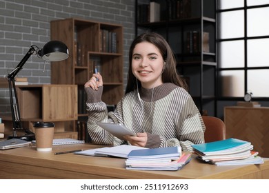 Female student with earphones and tablet computer studying at table in library - Powered by Shutterstock