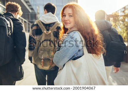 Female student glancing back while going for a class in college. Girl walking with friends going for class in high school.