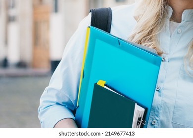 female student holding a folder and a notebook in her hands on a university background. Girl is taking exams at university