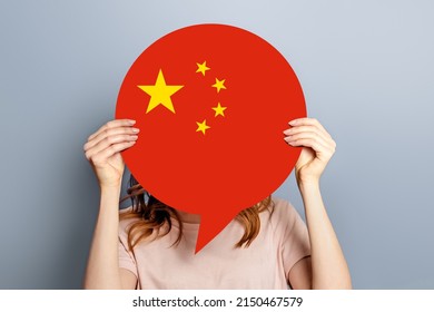 Female Student Holds Blank White Speech Bubble With Chinese Flag Isolated Over Grey Studio Background. Woman Holding A Round Information Piece Of Paper Dialog