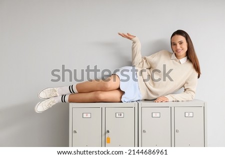 Female student lying on locker against light background