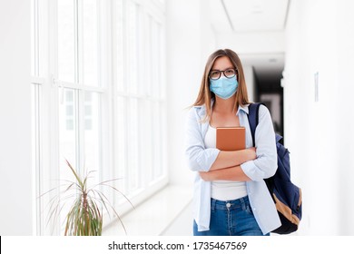 Female Student In Mask Indoors Going To Exams In High School. Young Woman In Empty University. Girl With Backpack And Book In College Corridor. Social Distancing During Quarantine.