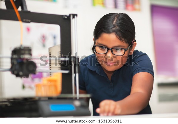 A female student in a modern classroom\
observing the printing process of a 3d\
model.