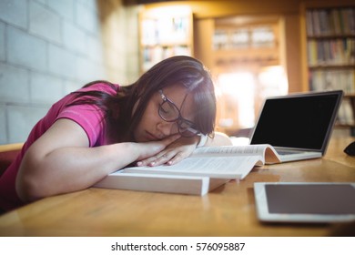 Female student napping on book at desk in library - Powered by Shutterstock