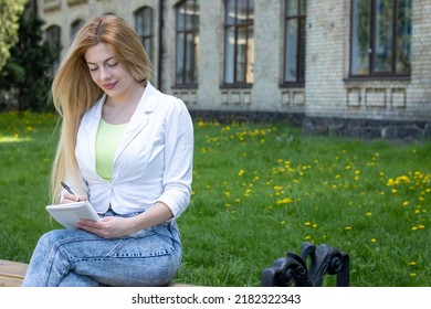 Female Student Sits On A Bench Near The Training Center And Makes Notes In A Notebook.