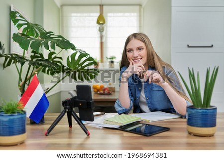 Female student sitting at home studying online, looking at smartphone webcam