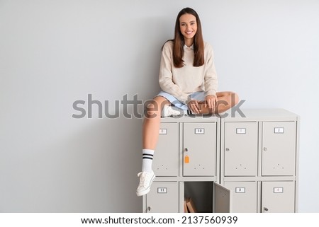 Female student sitting on locker against light background