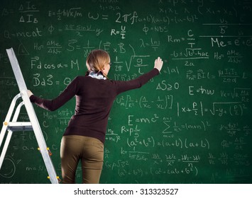 Female student standing on a ladder and writes on a chalkboard