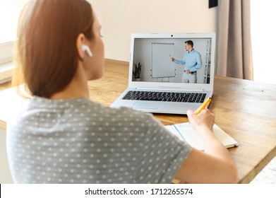 A female student studies online. A young woman is watching online classes and writing a syllabus in notebook. Concept of distance study, online learning, webinars. Back view