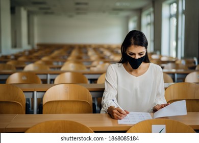 Female Student Taking An Exam Wearing A Protective Face Mask In An Empty Amphitheater. Stressed Student During COVID-19 Outbreak.Coronavirus In-class Test. Concerned Woman Having Education Evaluation