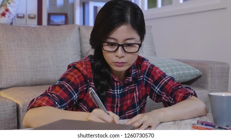 Female Student Taking Notes From A Book At Home. Young Asian Woman Sitting On Floor Assignments In Apartment Staying Up Late At Night. College Girl In Glasses Studying In Midnight Lifestyle.