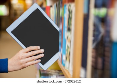 Female student tidying a tablet in a bookshelf in the library at the university
