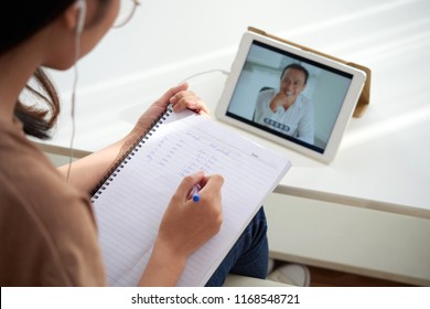 Female student watching online lesson and taking notes in textbook