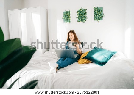 Female student watching video online webinar learn on laptop sitting on the bed with tea cup distance e-learning course video conference pc call in bedroom at home. Work from home, freelance concept.