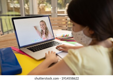 Female student wearing face mask having a video call with female teacher on laptop at school. distance learning online education during covid-19 concept - Shutterstock ID 1914558622
