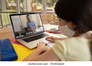 Female Student Wearing Face Mask Having A Videocall With Male Teacher On Laptop At Home. Distance Learning Online Education During Covid-19 Pandemic Concept