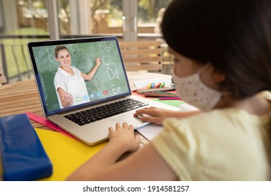 Female Student Wearing Face Mask Having A Video Call With Female Teacher On Laptop At School. Distance Learning Online Education During Covid-19 Concept