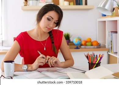 Female student at workplace portrait holding pen and looking in textbooks studying. Woman writing letter, list, plan, making notes, doing homework. Education, self development and perfection concept
