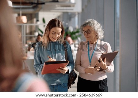 Female student writing notes while communicating with university professor after a lecture. 