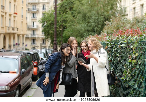 Female students\
speaking with curator and showing photos on tablet outdoors in  .\
Concept of sharing positive emotions and resting with teacher.\
Young girls smiling.