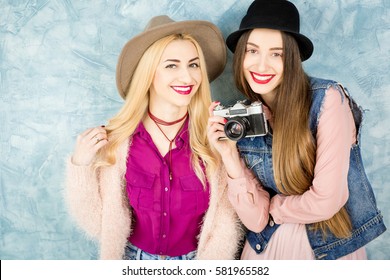 Female stylish friends having fun with photo camera on the blue wall background
