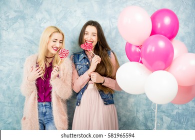 Female stylish friends having fun with candy and baloons on the blue wall background