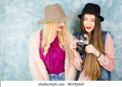 Female stylish friends having fun with photo camera on the blue wall background