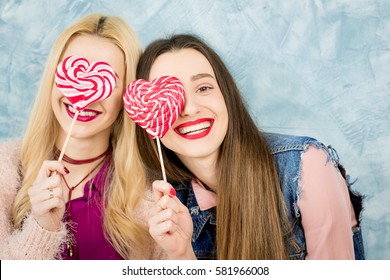 Female stylish friends having fun with candy on the blue wall background