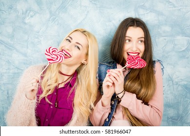 Female stylish friends having fun with candy on the blue wall background