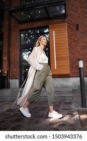 Female Stylish Model Walking City Street. Fashion Woman Blogger Wearing Fashionable Spring Or Autumn Clothes (beige Trench Coat, Oversize Khaki Cargo Pants, Accessorie) Outdoors. Trend Street Outfit