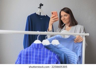 female stylist picks up clothes in wardrobe, talks on phone and takes photos of dress. shirts jacket bright color. recycling textile storage or shopping. - Shutterstock ID 2258605305