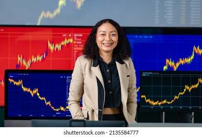 Female Successful Professional Broker Trader Investor Stand Smile Put Hands In Pants Pocket Look At Camera In Front Computer Monitor Screen With Stock And Bitcoin Cryptocurrency Graph Chart Analysis.