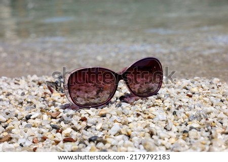 Female sunglasses on pebble stones on sea background. Beach vacation, tanning and swimming in summer