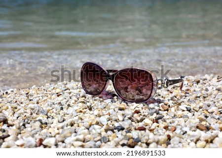 Female sunglasses on pebble stones on sea background. Beach vacation, tanning and swimming in summer