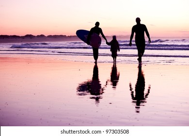 Female Surfer And Her Familly Walking In The Beach At The Sunset