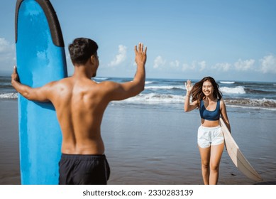 female surfer meets male friend by waving while walking with surfboard after practicing - Powered by Shutterstock