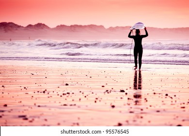 Female Surfer On The Beach At The Sunset