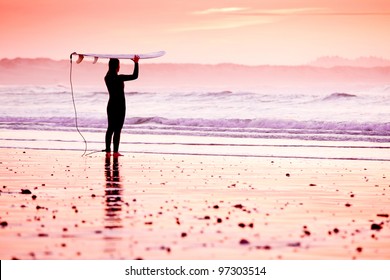 Female Surfer On The Beach At The Sunset