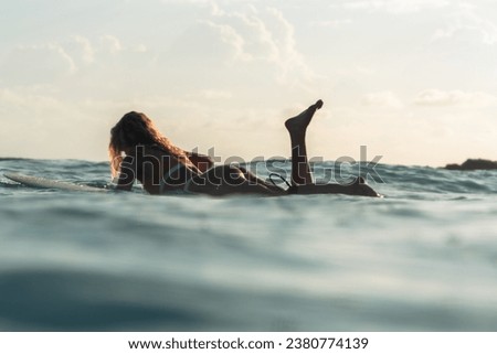 Female surfer paddling a surfboard on the ocean early in the morning
