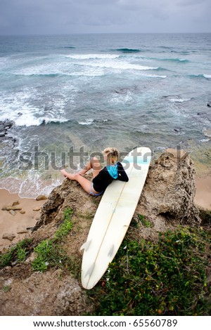 Female surfer sitting on cliffside with surfboard