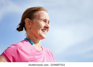 Female Surfer Wearing Bathing Suit And Pink Rashguard Looks Out Into The Sunny Day To The Right With Wet Hair And Skin                               