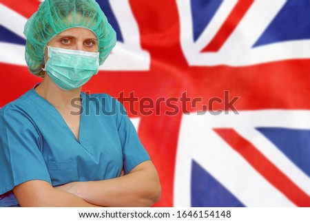 Female surgeon in mask and hat looks at the camera on the background of the United Kingdom flag. Health care and medical concept. Surgery concept and fight the virus in UK.