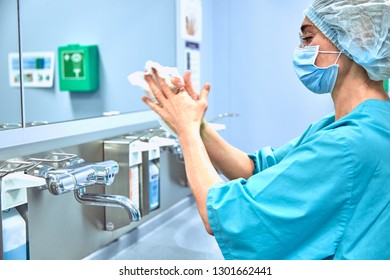 Female Surgeon in a medical mask and in a suit in the hospital washing thoroughly her hands before performing a surgery - Powered by Shutterstock