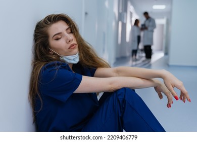 A Female Surgeon Is Sitting On The Floor Tired After A Long Operation. Huge Workload Of Hospitals During The Pandemic.